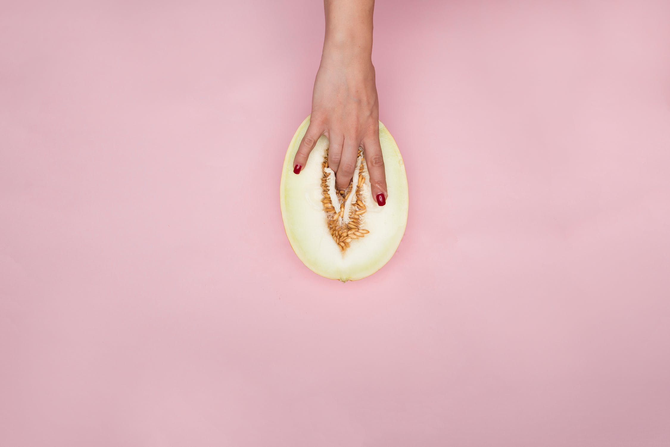 Photo of a hand with red fingernails touching a cut melon in a suggestive manner